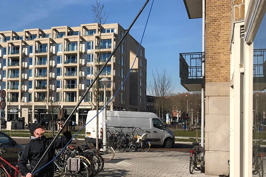 Glazenwasser werkt met een telescoopsteel aan ramen van een appartementencomplex